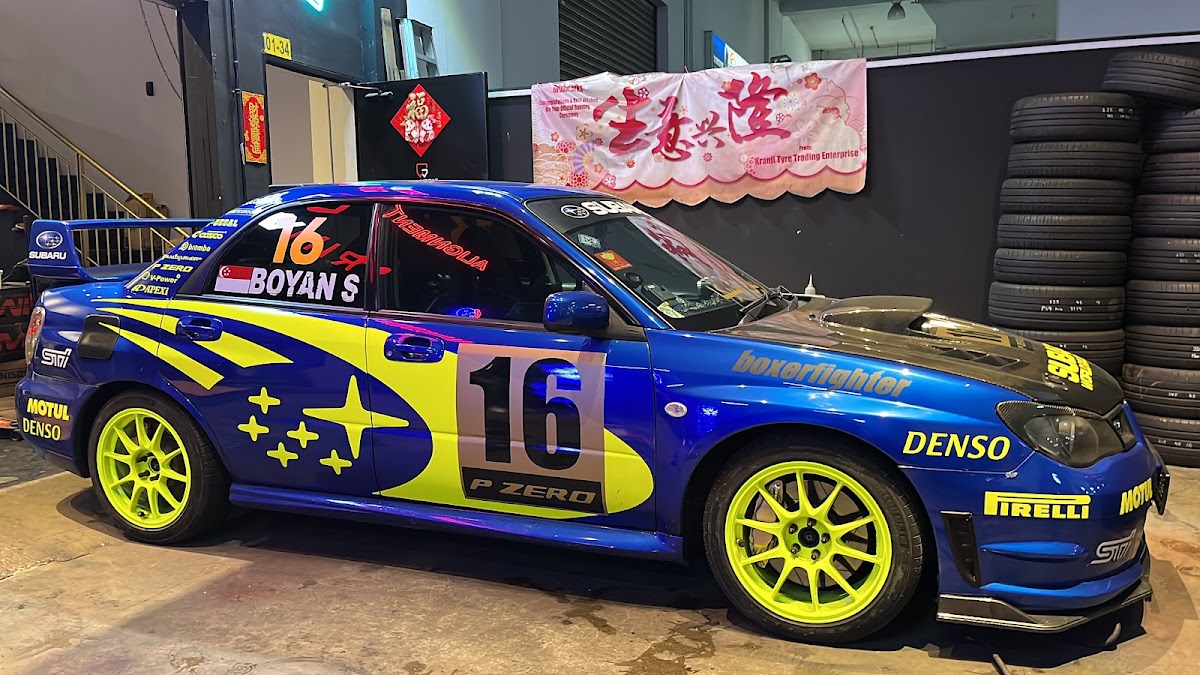 Blue Subaru rally-style car with neon yellow rims inside the workshop